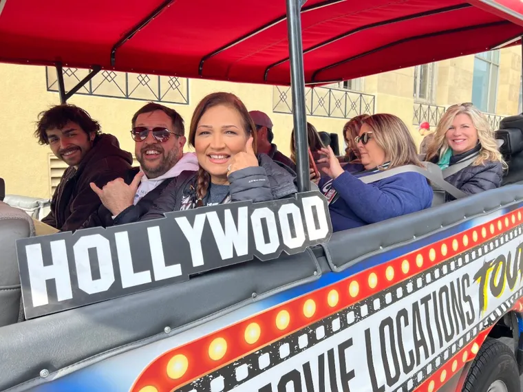 Corporate team enjoying the Film Freak Hollywood team building tour — laughing and posing with a Hollywood sign prop on the open-air van